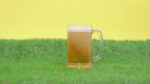 Cold refreshing foam beer is poured into large mug, cup stands on green grass of Stock Footage 138980397