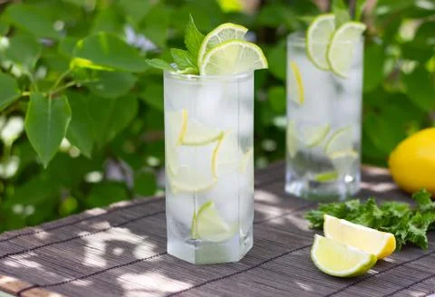 Cold refreshing lemonade or mojito coctail in a glass on gray bamboo and green Stock Photos