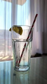 Cold Refreshing Water With Lemon Slice And Straw On Glass Table By Open Windo Fotos de archivo