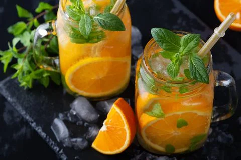 Cold summer orange lemonade with mint and ice in a glass. Stock Photos