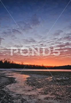 A cold sunset in winter on a frozen lake with a beautiful sky and sunbeams in Stock Photos