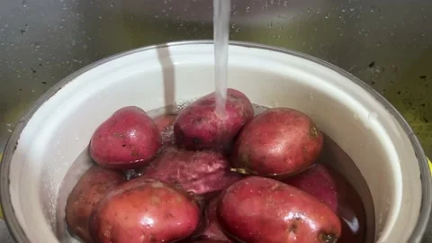 Cold tap water is poured into pot filled with red fresh raw potatoes Stock Footage 230087946