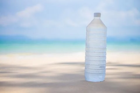 Cold water bottle with drops on it on tropical island beach Stock Photos