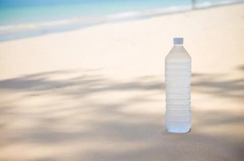 Cold water bottle with drops on it on tropical island beach Stock Photos