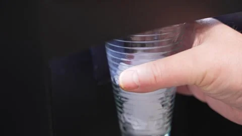 Cold water with ice is dispensed into a clear plastic cup from a refrigerator Video stock 328650828