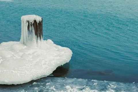 Cold weather causes ice to form around a wooden post at the edge of the water Stock Photos