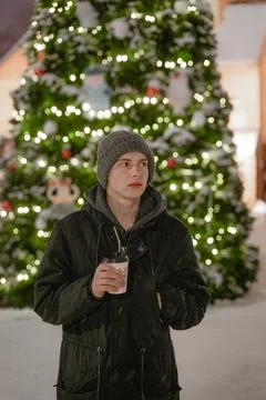 In cold winter drinks a hot drink by the Christmas tree, in winter clothes in Stock Photos