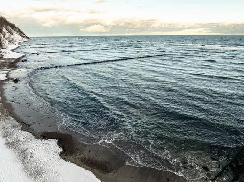 Cold winter waves gently lap against the sandy beach mixing with gravel and s 写真素材