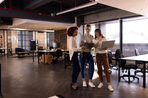 Collaborating in modern office, three multiracial women discussing work using 스톡 사진