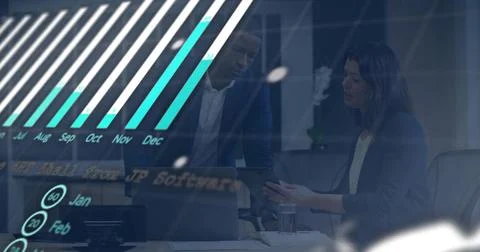 Collaborating pair in dark suits leaning over laptop in office with tablet, Fotos Stock