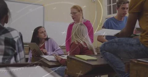 Collaborating students pointing at tablet screen in classroom, passing papers at Stock Photos