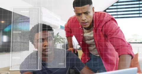 Collaborating two men in navy tee, red shirt reviewing laptop screen at office, Stock Photos