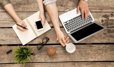 Collaboration at a wooden table with laptops, notebooks, and smartphones during Stock Photos