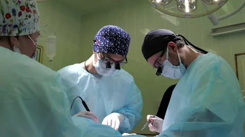 Collaborative surgical team performing precise operation beneath overhead lights Stock Footage 340526935
