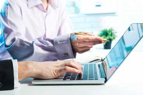 Collaborative work session takes place in a bright office with a laptop and two Stock Photos