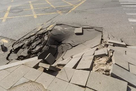 Collapsed asphalt and broken sidewalk blocks expose dangerous road damage at Stock-Fotos