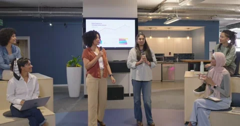 Colleagues clapping in open-plan lounge, sending two women presenting charts Stock Footage 343887488