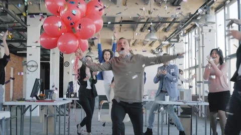 Colleagues congratulate the young manager. They give him red balloons, ride them Stock Footage 124485554