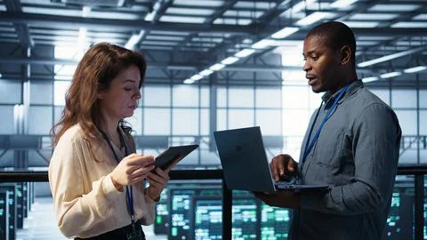 Colleagues in data center workplace use laptop to calibrate energy usage Stock Photos