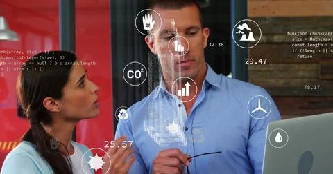 Colleagues examining floating code and CO? icons at desk, with laptop and Stock Photos