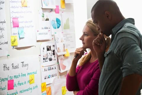 Colleagues looking at adhesive notes and paper on wall Stock Photos