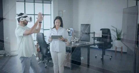 Colleagues manipulating interface in office near grid window, wearing VR headset Stock Photos