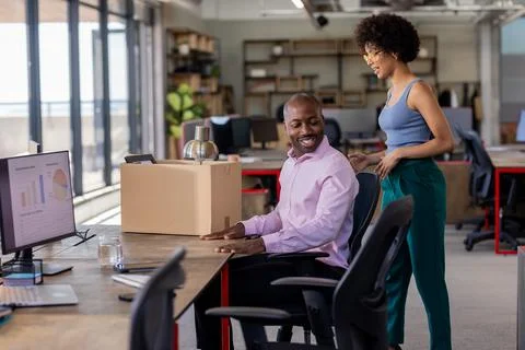 Colleagues in office smiling while unpacking box at desk with computer Stock Photos
