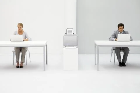 Colleagues in office using laptop computers, printer between them with graphic Stock Photos