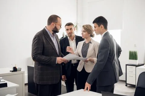 Colleagues stand with the documents and look at their chief in the office Stock-Fotos
