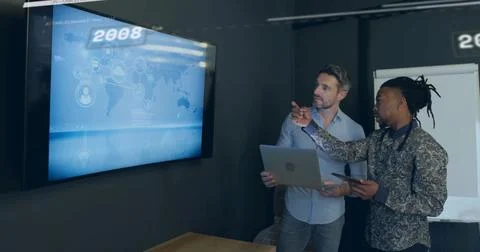 Colleagues studying network map on flat screen in office, with laptop, tablet, Foto stock