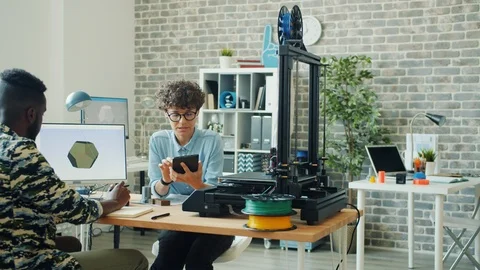 Colleagues using tablet, computer and 3d printer in office talking working Stock Footage 119554093