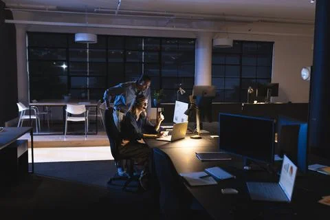Colleagues working late in office, analyzing data on computer screen together Foto stock