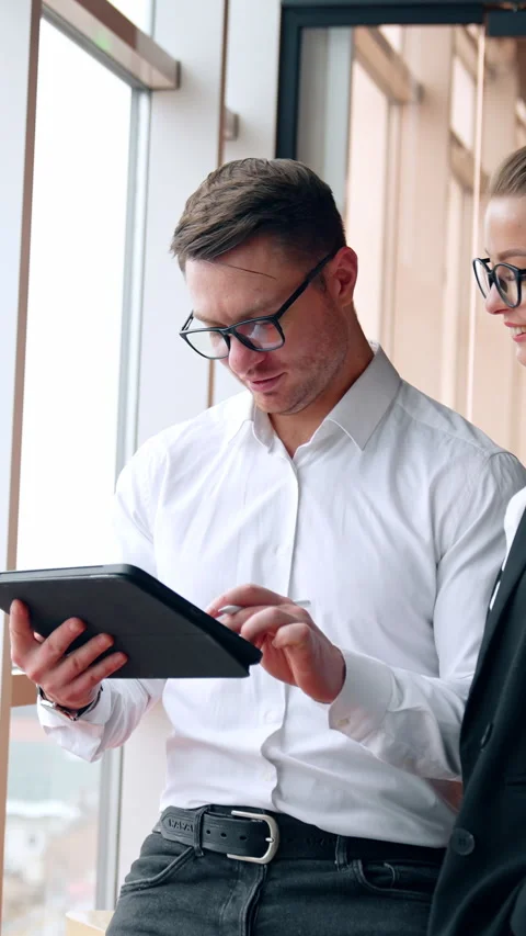 Colleagues working in office stand at the window. Man uses I-pad and woman Stock Footage 325040562