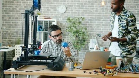 Colleagues young men talking in office using 3d printer, tablet and laptop Stock Footage 119762573