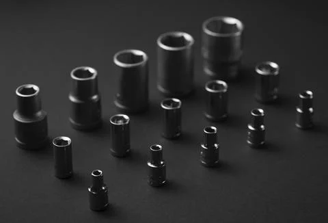 A collection of black chrome socket extensions is arranged on a dark gray Stock Photos