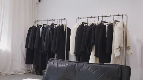 A collection of clothes in a store hangs on hangers against a white wall. Stock Footage 306666076
