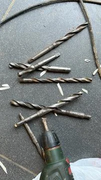 A collection of old, used metal drill bits scattered on a dark grey tiled floor Stock Photos