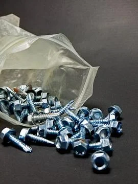 A collection of silver-colored hex head screws spills from a plastic bag on.. Stock Photos