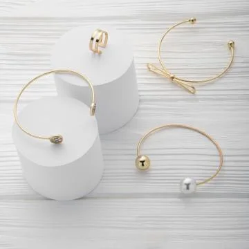 Collection of three bracelets and ring on white platforms on wooden backgroun Foto stock