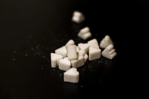 A collection of white sugar cubes with various shapes scattered on a black 库存照片