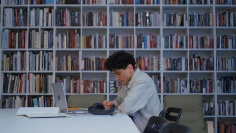 College Guy Studying from Physical Book and Digital Device in Book-Filled 스톡 동영상 335123962