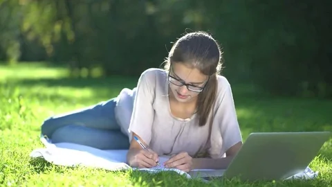 College student lying down on the grass and working on laptop, tracking shot Video stock 69187234