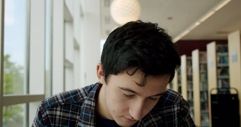 College student sitting in library, writes in a notebook, then looks at the Stock Footage 125958029