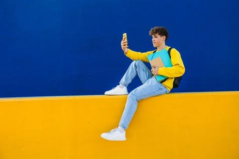 College student taking a selfie while holding folders and sitting on a colorful Stock Photos