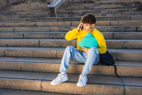 College student talking on smartphone while sitting on stairs outdoors Stock Photos