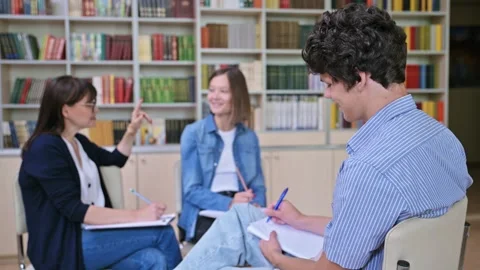 College students discussing their studies with female teacher inside library Stock Footage 248455688