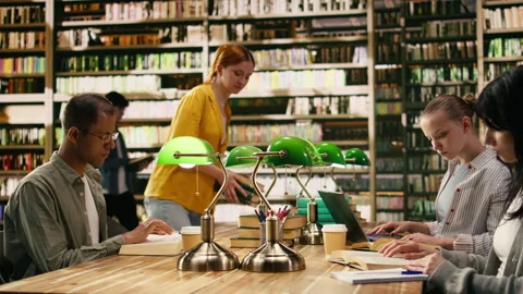 College students sitting in library reading books and using laptop Stock Footage 336358281