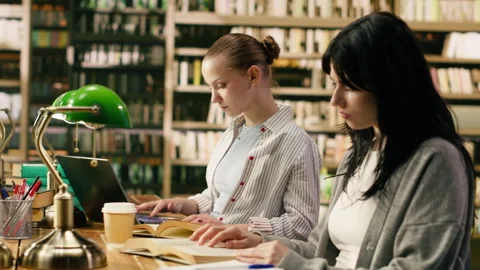 College students sitting in library reading books and using laptop Stock Footage 336360168
