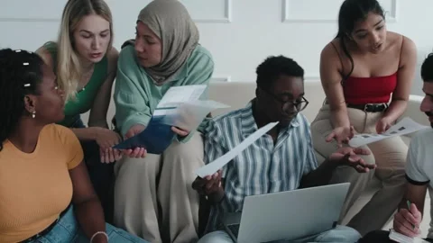 College students sitting together on sofa, using laptop computer, papers books Stock Footage 251537398