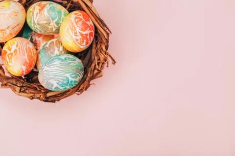 Coloeful easter eggs in nest on pastel pink color background. Stock Photos